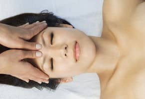 Eine asiatische Frau mit geschlossenen Augen erhält eine Anti Migräne Massage.