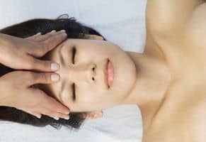 anti migräne massage Eine asiatische Frau mit geschlossenen Augen erhält eine Anti Migräne Massage.
