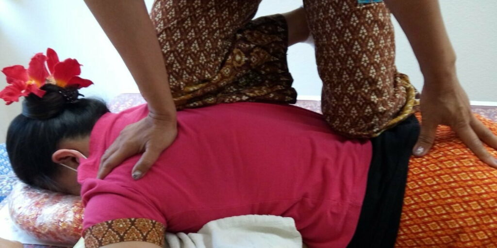 Eine Thai Masseurin kniet auf einer Patientin und demonstriert die kraftvolle Energie der thailändischen traditionellen Massagetechniken.