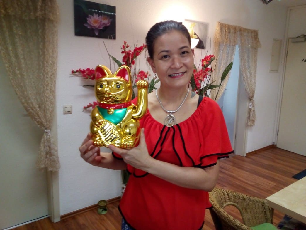 Kitty Kammer von Kitty's Thai Massage hält eine goldene thailändische Glückskatze in die Kamera.