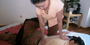 Ein Thai Masseurin kniet über einem Patienten, um ihn zu dehnen.