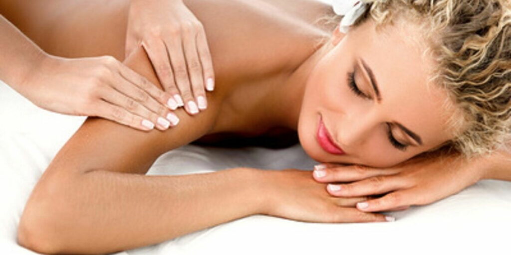 Einer jungen blonden Frau werden vorsichtig die Oberarme massiert. Dies gehört zu einer wohltuenden und entspannten Ganzkörper Wellnessmassage.